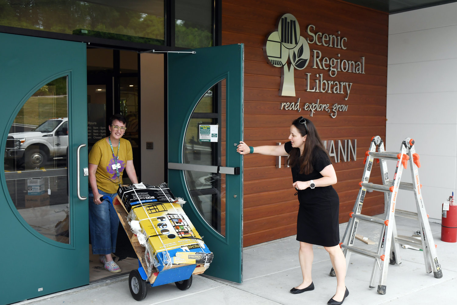 Scenic Regional Library staff members Christy Schink (left), associate director of youth and outreach services, and Megan Maurer, assistant director, move a wheel cart load of supplies on Friday morning into the newly created facility in Hermann.