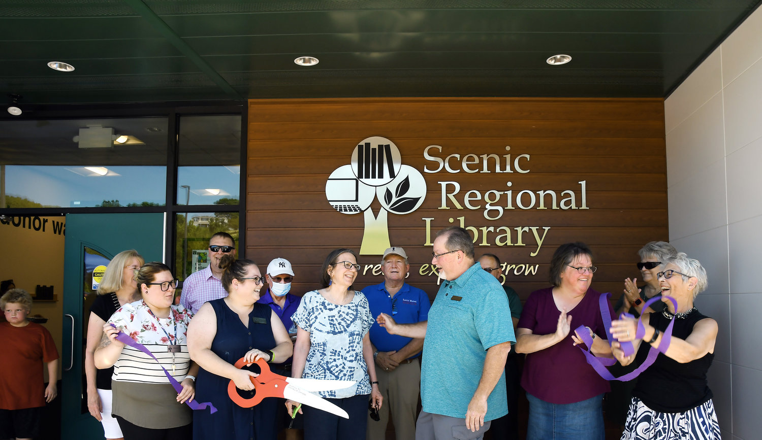 Hermann Area Chamber of Commerce President Gary Watts congratulates Scenic Regional Library trustee Kathi Ham (center, of Hermann) after the ceremonial ribbon cutting Saturday during grand-opening festivities of the Hermann branch. Also pictured (from left) are Karen Holtmeyer, (library trustee), Makayla Baker (branch employee), Steven Campbell (Scenic Regional’s executive director), Kasey Wright (manager of the Hermann and New Haven library facilities), John Barry (trustee), Larry Miskel (Gasconade County presiding commissioner), Dan McKinney (executive director of Hermann Area District Hospital), Carla Robertson (trustee), Linda Andrea (in corner, trustee), and Sheri Hausman (former Hermann branch manager, now volunteer manager of the library’s art gallery). Hausman has worked for the library system for 33 years.